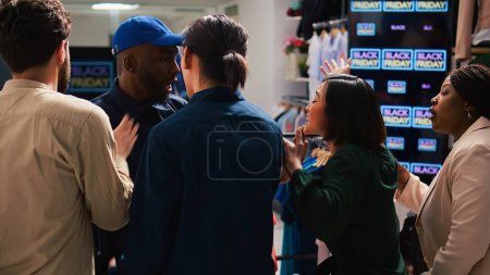 Photo for Security officer calms crowd on black friday sales rush, pushing people back and trying to control clothing store entrance. Clients shoppers being impatient, obsessed with cheap prices. - Royalty Free Image