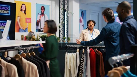 Photo for Happy customer at checkout counter in retail store, buying new clothes during black friday event. Young man carrying stander full of clothing items and accessories, seasonal sales obsession. - Royalty Free Image