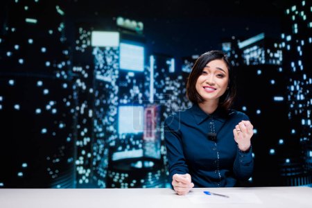 Photo for Night show host on live broadcast addressing global news topics from newsroom, discussing about daily events. Asian presenter reporting media information to provide latest tv content. - Royalty Free Image