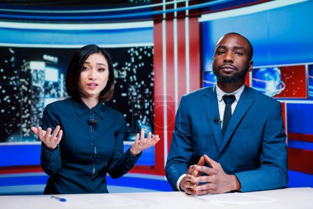 Talk show hosts reading breaking news headlines live on television broadcast, working together to provide relevant content for tv program. Diverse team of reporters in newsroom.