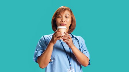 BIPOC nurse tasting instant coffee while at work, surprised by unexpected aroma. Close up shot of hospital employee drinking hot beverage with unusual aftertaste, isolated over studio background