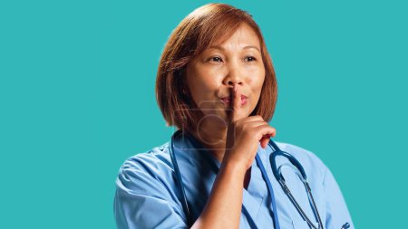 Close up shot of rigid strict BIPOC clinic manager shushing at camera, bothered by too much noise. Rigurous nurse holding quiet gesture finger to lips, isolated over studio background