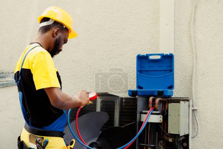 Photo for Proficient african american worker doing routine condenser maintenance, assembling manifold indicators before starting work. Qualified electrician getting equipment ready to check freon leaks - Royalty Free Image