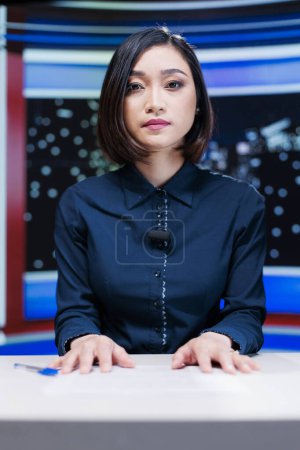 Photo for Presenter on midnight news show addressing media outlets information about international events during live segment. Asian woman talking about international newscast with details. - Royalty Free Image