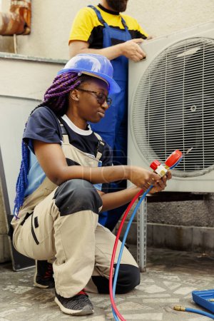 Close up of african american engineer holding manifold gauges used for checking air conditioner freon levels. BIPOC technician using barometer, checking refrigerant levels of hvac system