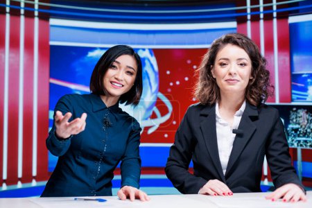 Photo for Journalists team discuss daily news, presenting latest events on international television program in newsroom. Two women broadcasters working on entertainment segment with reportage. - Royalty Free Image