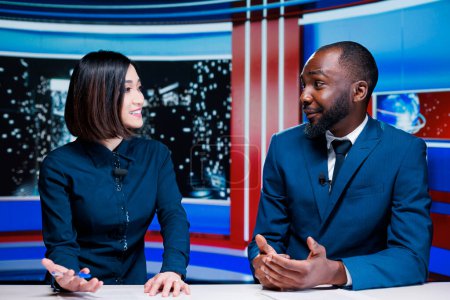 Two reporters broadcasting live information on international television channel, addressing all latest events and giving updates. Diverse presenters creating tv content in studio.