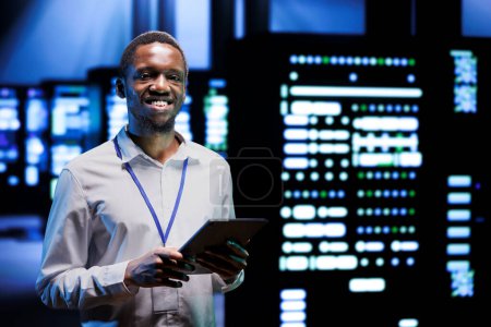 Portrait of smiling overseerer running data center devices diagnostic tests to determine and debug software problems. Happy serviceman using tablet to analyze critical systems, checking for crashes