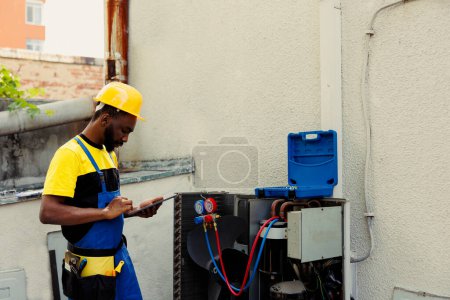 Photo for Competent mechanic doing air conditioner checkup, looking for leaks and other necessary repairs to prevent major breakdowns. Adept repairman troubleshooting condenser, writing findings on clipboard - Royalty Free Image