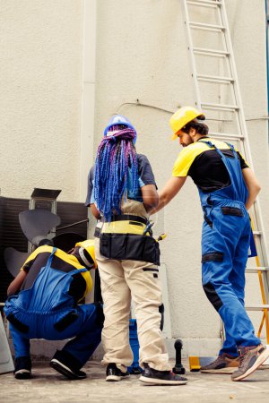Photo for Diverse team of competent mechanics working outside, checking for jammed air filters hindering hvac system airflow, causing heating system to work harder and consume more energy - Royalty Free Image