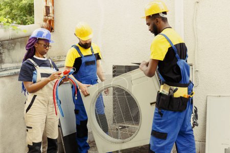 Ingenieros capacitados encargados por el propietario de la casa para buscar fugas de refrigerante en la bobina del evaporador del acondicionador de aire externo que conducen a problemas de enfriamiento pobres durante los meses de verano calientes