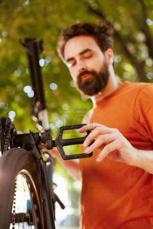 Photo for Sports-loving dedicated man repairing bicycle parts using professional tools in home yard. Healthy caucasian male cyclist assessing and mending damaged bicycle as summer activity. - Royalty Free Image