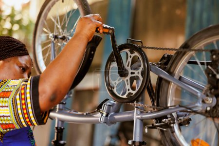 Leidenschaftliche, sportbegeisterte schwarze Frau inspiziert und repariert fleißig Fahrradpedale und -ketten. Aktive afrikanisch-amerikanische Radfahrerin macht jährliche Anpassungen an modernes Fahrrad.