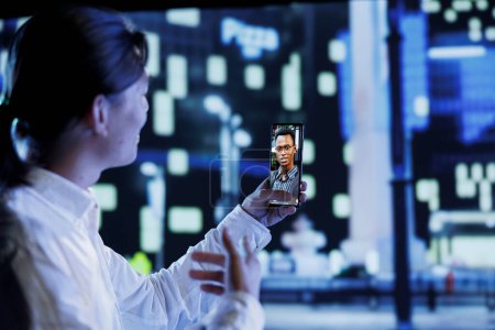 Asian man in videocall with step brother while walking around city avenues at night, giving him work updates. Person uses smartphone to show sibling dimly illuminated cityscape