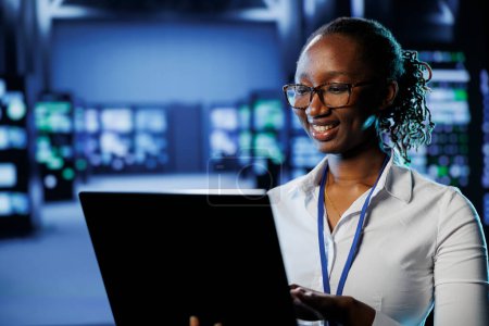 African american woman between server farm rows providing processing resources for businesses worldwide. Admin fixing data center rackmounts tasked with managing massive databases