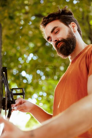 Photo for Committed healthy and energetic man adjusting and securing bicycle parts for enjoyable summer cycling. Young male caucasian cyclist repairing bike wheel as yearly maintenance outdoors. - Royalty Free Image