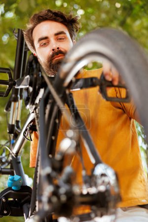 Gros plan d'un homme caucasien amateur de sport travaillant dans sa cour pour réparer des pièces de vélo avec un outil spécialisé. Image détaillée du jeune cycliste mâle inspectant et ajustant la roue et la pédale du vélo.