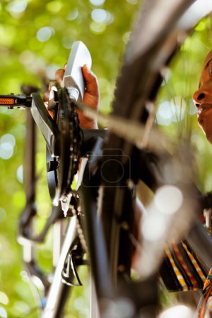 Photo for African american woman greasing and servicing modern bicycle chain for yearly summer maintenance. Detailed image showing female hand skillfully lubricating bike pedals outdoors. - Royalty Free Image