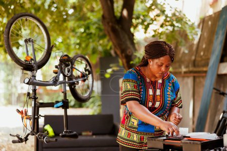 Photo for Committed sports-loving black woman outside utilizing toolbox for expert bicycle repair. Young healthy african american female working on damaged bike with professional equipments. - Royalty Free Image