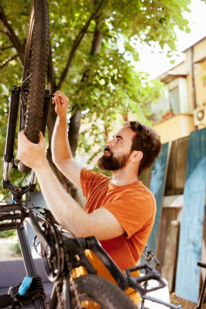 Photo for Fit and active male cyclist fastening bike tire safely for outside cycling. Dedicated caucasian man performing bike maintenance skillfully fixing bicycle wheel with essential work tool. - Royalty Free Image