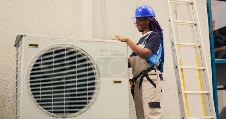 Photo for Efficient repairman starting work on defective air conditioner, using handheld drill to disassemble condenser metal coil panel. Experienced mechanic dismantling hvac system to check for dirt - Royalty Free Image