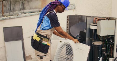 Proficient worker starting comission on defective air conditioner, meticulously disassembling condenser metal front coil panel. Capable electrician dismantling hvac system to check for dust