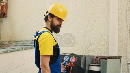 Meticulous technician commissioned for annual air conditioner maintenance, assembling manometer before starting work. Trained worker checking freon leaks leading to reduced cooling efficiency