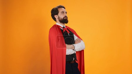 Photo for Powerful comic superhero with red cape standing against yellow background, feeling strong on camera. Dedicated valet superhuman with mantle working in restaurant dining industry. - Royalty Free Image