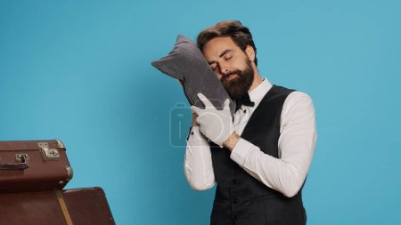 Sleepy bellman posing with pillow in studio, advertising burnout and being overworked in classy hospital industry. Hotel porter taking quick nap after working overtime, tired doorman.