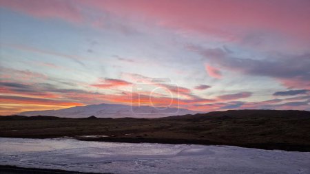 Téléchargez les photos : Ciel rose incroyable pendant le coucher du soleil en iceland, couvrant les montagnes et les champs gelés dans la région nordique. Paysage scandinave spectaculaire avec ciel de barbe à papa, aventure de l'heure dorée. - en image libre de droit