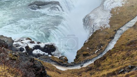 Cascada Gullfoss en la región de hielo, majestuoso flujo de ríos helados y colinas cubiertas de nieve. Paisaje nórdico con cascada masiva y arroyo de agua que desciende junto a las colinas y los bordes.