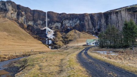 Foss una cascada Sidu y casa de campo en Islandia, que vierte desde el borde de la colina y la creación de un paisaje natural idílico. Magnífica cascada nórdica con chorro de agua cayendo de pendientes.
