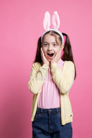 Téléchargez les photos : Enfant positif enthousiaste agissant surpris par les cadeaux de Pâques en studio, se sentant joyeux avec ses cadeaux et profiter de la fête d'avril. Jeune enfant optimiste excité par la célébration du printemps. - en image libre de droit