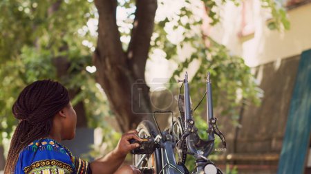Femme noire énergique détachant pneu de vélo endommagé pour la fixation et le changement avec nouveau. Femme africaine américaine athlétique saine saisissant et retirant la roue de vélo pour plus d'entretien.
