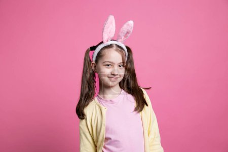 Photo for Young confident girl with pigtails and bunny ears posing on camera, feeling happy and joyful about easter celebration. Little kid being adorable over pink background, festive spring holiday. - Royalty Free Image