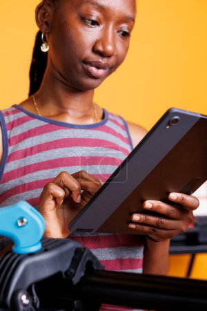 Photo for Dedicated black woman searching on internet using phone tablet to research on bike maintenance. Close-up of healthy active female cyclist grasping smart device with instructions for fixing bicycle. - Royalty Free Image
