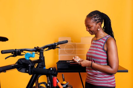 Sportbegeisterte Frau wählt und untersucht verschiedene Werkzeuge aus dem professionellen Werkzeugkasten für die Fahrradwartung. Afrikanische Radfahrerin greift nach Spezialausrüstung für die Reparatur von Fahrrädern.