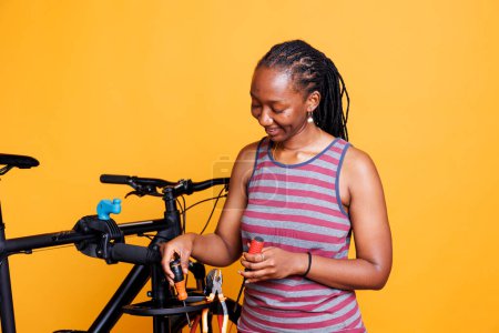 Junge afrikanisch-amerikanische Dame bereitet grundlegende Werkzeuge für die Reparatur beschädigter Fahrräder vor. Sportliche schwarze Frau ergreift vor isoliertem Hintergrund mehrere Spezialgeräte zur Reparatur kaputter Fahrräder.