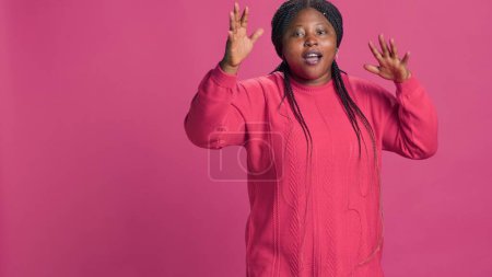 Young black woman displeased and saying no at camera with hands raised. African american fashion blogger having disappointed self expression positioned against pink background.