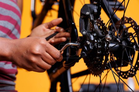 Nahaufnahme einer schwarzen Person, die ein Fahrrad fachmännisch repariert, indem sie ein Arbeitswerkzeug benutzt, um verschiedene Komponenten anzupassen. Fotofokus auf afrikanisch-amerikanische Handgriffe verstellbares Multifunktionswerkzeug für die Fahrradwartung.