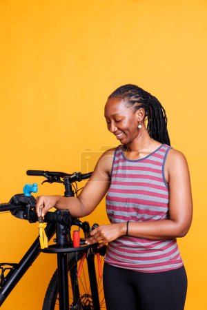 Foto de Ciclista femenina enérgica que agarra herramientas de trabajo esenciales para inspeccionar y reparar bicicletas. Mujer afroamericana activa sosteniendo y colocando alicates, destornilladores y otros equipos para el mantenimiento de bicicletas. - Imagen libre de derechos