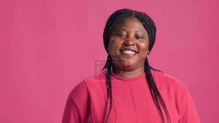 Video showcasing stylish african american woman with penchant for pink sweater fashion confidently striking poses. Genuine laughter of young lady infuses authentic charm to the close-up shot.