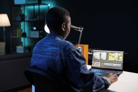 Afroamerikanische Filmemacherin vertieft in ihren Personal Computer, bearbeitet und erstellt multimediale Inhalte. Bild zeigt eine schwarze Frau, die am digitalen Laptop sitzt und arbeitet und Filmmaterial analysiert.