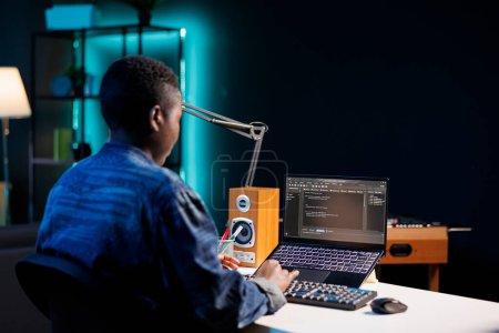 Foto de La programadora negra trabaja en su computadora personal, administrando la base de datos y monitoreando la red de seguridad cibernética. Mujer afroamericana sentada en el escritorio y usando un portátil digital para codificar. - Imagen libre de derechos
