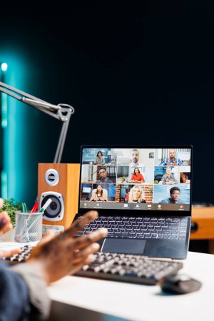 Vue détaillée de l'écran d'ordinateur portable affichant un groupe de personnes lors d'une vidéoconférence. Afro-Américain travaillant à la maison, ayant une communication virtuelle avec ses collègues sur un ordinateur sans fil.