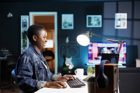 Mujer negra sonriente manejando un sistema complejo usando el aprendizaje automático en su computadora personal. Alegre programador afroamericano sentado y escribiendo en código para crear base de datos en el ordenador portátil.