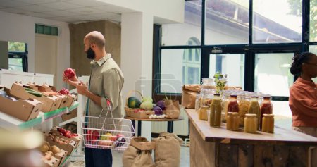 Der Kunde betrachtet Bio-Früchte und Gemüse in Kisten und kauft Bio-Gemüse, um vegane Mahlzeiten zuzubereiten. Junger Erwachsener in lokalem, umweltfreundlichem Supermarkt sucht nach chemikalienfreien Lebensmitteln.