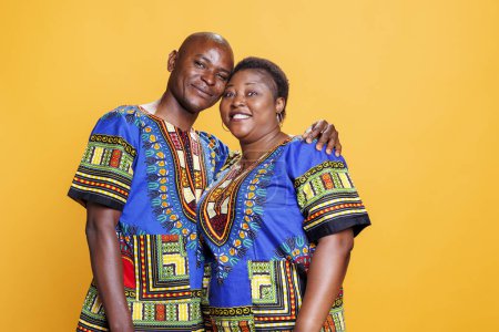 Photo for Smiling black man and woman couple dressed in ethnic clothes embracing, showing love and happiness studio portrait. Wife and husband and looking at camera with cheerful expression - Royalty Free Image