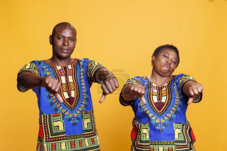 Mann und Frau zeigen Daumen nach unten Geste, während negative Bewertung Porträt. Afroamerikanisches Paar posiert mit Abneigung, zeigt schlechtes Feedback und blickt in die Kamera