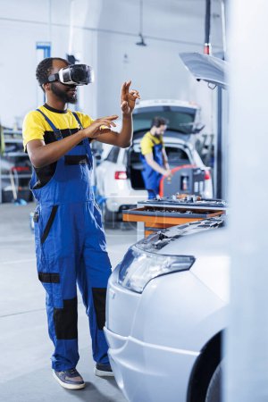 Photo for Specialist in auto repair shop using virtual reality to visualize car lights system in order to fix it. Knowledgeable garage worker wearing futuristic vr headset while repairing faulty vehicle - Royalty Free Image